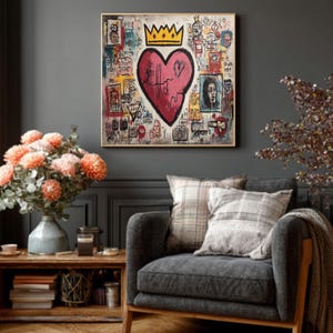 May include: A framed artwork featuring a pink heart with a crown, surrounded by graffiti-style drawings and text. The painting hangs above a gray armchair with plaid pillows, a wooden side table, and a vase of orange flowers.