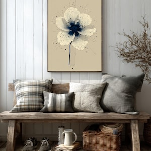 May include: A framed floral art print featuring a white flower with a dark blue center and stem. The artwork is displayed above a wooden bench with pillows, shoes, and a basket. The color palette includes beige, white, and brown.