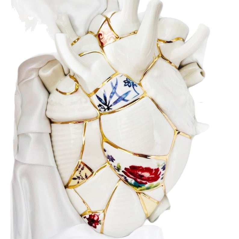 May include: A white ceramic heart sculpture, artfully pieced together with gold accents, showcasing floral and patterned designs. The heart's broken sections are meticulously rejoined, creating a unique decorative piece.