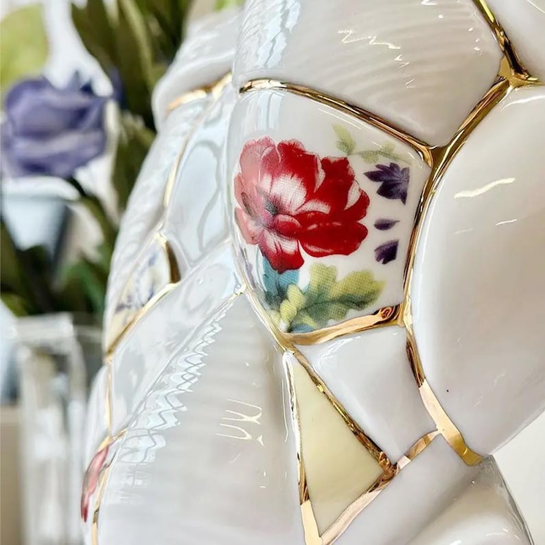 May include: Close-up of a white ceramic vase with a mosaic design, featuring a red floral pattern. The mosaic pieces are outlined with gold trim. The vase has a unique, artistic appearance, suitable for home decor.