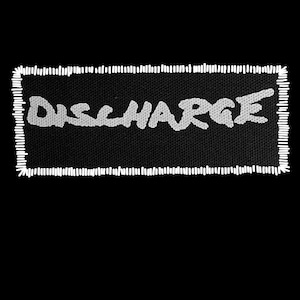 May include: A black rectangular patch with the word "DISCHARGE" in white, stylized lettering. The patch has a white stitched border, and the background is solid black.