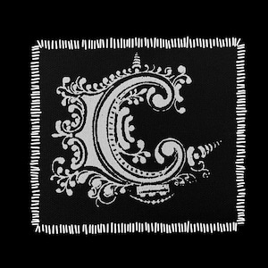 May include: Black square patch with a white, ornate letter "C" in a vintage style. The letter is surrounded by decorative flourishes and a stitched white border. The patch is suitable for clothing or accessories.