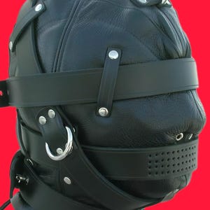 Pu&ograve; includere: Cappuccio in pelle nera con design trapuntato, elementi metallici e cinghie regolabili. Presenta un grande anello metallico sulla parte superiore e una sezione perforata vicino alla bocca. Il cappuccio &egrave; progettato per coprire l'intera testa e il collo.