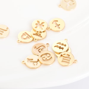 Könnte beinhalten: Goldfarbene Metallanhänger mit verschiedenen Tierkreiszeichen. Jeder Anhänger ist eine kleine, runde Scheibe mit einem ausgeschnittenen Design, das ein anderes astrologisches Zeichen darstellt. Die Anhänger haben kleine Schlaufen zum Befestigen an Schmuck oder anderen Bastelarbeiten.