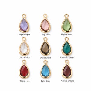 May include: Nine teardrop-shaped charms with gold-toned metal settings and faceted glass stones in light purple, deep pink, light green, clear white, olive green, emerald green, bright red, lake blue, and coffee brown, each with a small jump ring.