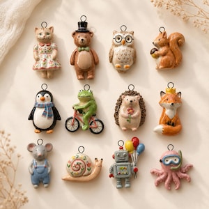 May include: A collection of twelve ceramic animal and character ornaments, each with a small metal loop at the top. The figures include a cat in a floral dress, a bear in a top hat, an owl with glasses, a squirrel, a penguin, a frog on a bicycle, a hedgehog, a fox with a crown, a mouse in overalls, a snail, a robot with balloons, and an octopus with a snorkel.