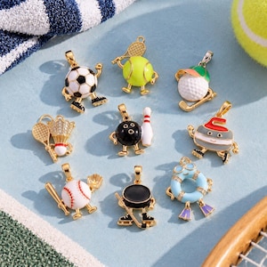 May include: A collection of nine gold-tone metal charms featuring various sports themes, including a soccer ball, tennis ball with racket, golf ball, badminton shuttlecock, bowling ball with pin, curling stone, baseball with bat, hockey puck with stick, and a life preserver.