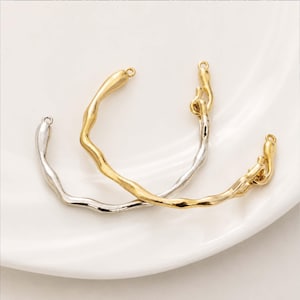 May include: Two metal jewelry components with an organic, wavy design. One is silver-colored, the other is gold-colored. Each has a loop at the top for attaching to other jewelry pieces. The components are displayed on a white surface.