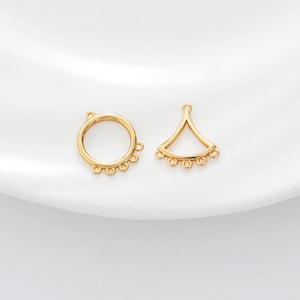 May include: Two gold-colored jewelry components. One is a circle with multiple small loops around the edge. The other is a fan-shaped piece with a loop at the top and multiple small loops along the bottom edge. Both are on a white surface.