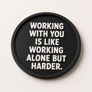 May include: A black round coaster with a raised edge. The white text reads: "WORKING WITH YOU IS LIKE WORKING ALONE BUT HARDER."