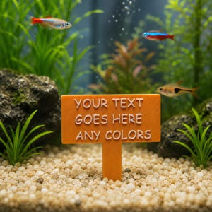 Peut inclure: Un panneau d'aquarium rectangulaire orange avec un piquet, présentant le texte blanc en relief "YOUR TEXT GOES HERE ANY COLORS" sur le devant. Le panneau est placé verticalement dans du gravier clair au fond d'un aquarium avec des plantes.