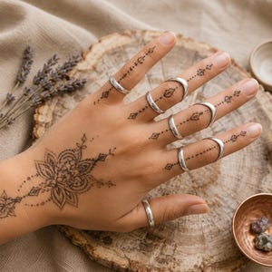 Può includere: Un set di sei anelli in argento liscio indossati sulle dita. Gli anelli sono lisci, lucidi e di forma circolare. Ogni anello è posizionato su un dito, con un anello sul pollice e cinque anelli distribuiti sulle altre quattro dita.