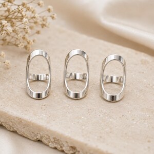 May include: Three silver-toned rings, each featuring a tall, vertical oval frame design. The rings have a smooth, polished metallic finish and a simple band structure that connects the base of the elongated oval shape to form a cohesive piece.