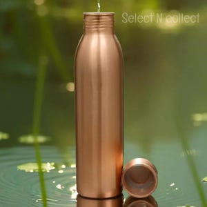 Puede incluir: Una botella de agua de color cobre con una tapa a juego, sobre un fondo verde borroso. La botella es cil&iacute;ndrica con un cuello estrecho y una tapa de rosca. El texto "Select N collect" es visible.