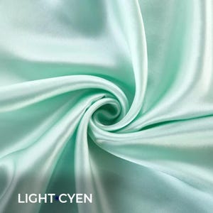 Könnte beinhalten: Nahaufnahme eines Wirbels aus helltürkisfarbenem Stoff. Der Stoff hat eine seidige, glatte Textur und einen leichten Glanz, mit dem Text "LIGHT CYEN" unten. Der Stoff ist gefaltet und verdreht, wodurch ein Spiraleffekt entsteht.