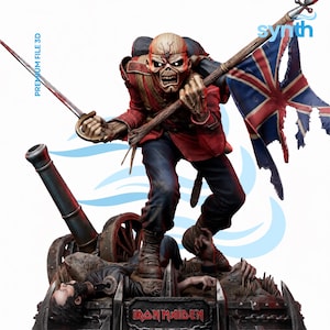 Op de afbeelding: Gedetailleerd beeldje van een skeletfiguur in een rode militaire jas en blauwe broek, met een zwaard en een verscheurde Union Jack-vlag. De figuur staat bovenop een kanon en gevallen soldaten. De tekst "IRON MAIDEN" is zichtbaar op de basis.