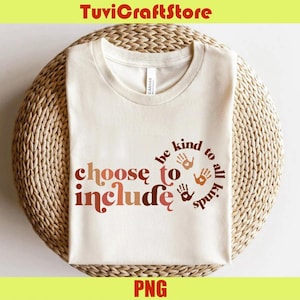 May include: Cream-colored t-shirt with the words "choose to include" in a retro font, and "be kind to all kinds" in a circular design. The design includes handprints in various shades of brown. The shirt is on a woven surface.