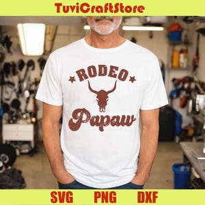 May include: White t-shirt with a brown graphic that reads "RODEO Papaw" with a bull skull design. The text is in a vintage style. The shirt is a casual wear item.
