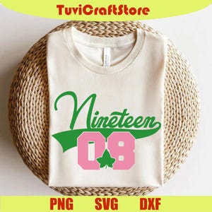 Puede incluir: Camiseta color crema con la palabra "Nineteen" en escritura verde y los números "08" en letras rosas. Una hoja verde está entre los números. La camiseta está sobre una superficie tejida. El texto "PNG SVG DXX" está en la parte inferior.