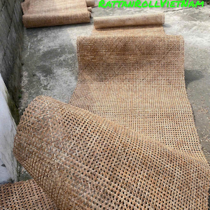 Könnte beinhalten: Mehrere Rollen gewebter Rattanmatten werden im Freien gezeigt. Die Matten sind hellbraun und haben ein rautenförmiges Muster. Der Text "RATTANROLLVIETNAM" ist grün zu sehen. Die Matten scheinen neu und unbenutzt zu sein.