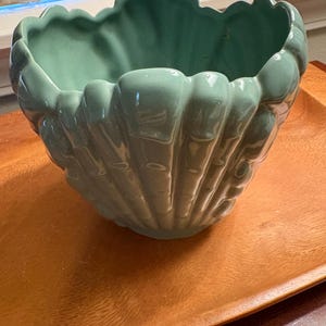 May include: A seafoam green ceramic planter shaped like a large seashell. The vessel features a scalloped rim and vertical ridges along the exterior, creating a textured, shell-like appearance with a smooth, glossy finish throughout the piece.