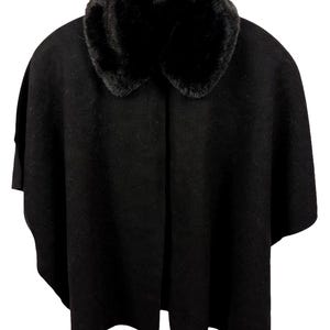 May include: A solid black cape featuring a thick, plush faux fur collar. The garment has a wide, open-front design with a smooth, felt-like texture throughout the main body, providing a structured drape that falls evenly from the shoulders.