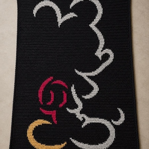 May include: A rectangular black crochet blanket featuring a stylized outline design. The pattern is created with light gray yarn forming a large curved shape, a red circular accent, and a yellow crescent moon shape at the bottom left corner.