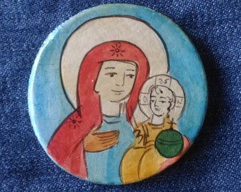 Könnte beinhalten: Eine runde, bemalte Keramikikone, die die Jungfrau Maria zeigt, die das Jesuskind hält. Die Ikone hat einen blauen Hintergrund mit einem weißen Heiligenschein um den Kopf der Jungfrau Maria. Die Jungfrau Maria trägt ein rotes Gewand mit goldenen Sternen und eine blaue Tunika. Das Jesuskind trägt ein gelbes Gewand und hält eine grüne Kugel.
