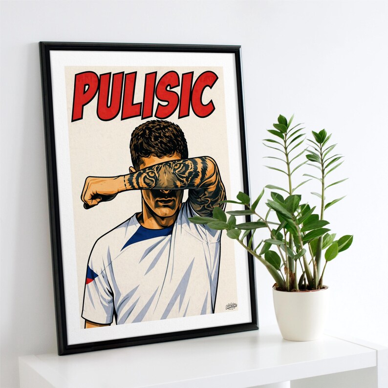 May include: A framed poster featuring a stylized illustration of a soccer player with the name PULISIC printed in large red letters at the top. The player wears a white jersey and has a prominent tiger tattoo on their forearm, which covers their eyes.