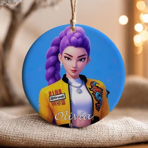 Peut inclure: Ornement rond en céramique avec un portrait stylisé d'une femme aux cheveux violets et une veste jaune. La veste porte le texte "RRItrumii" et un motif coloré. Le nom "Olivia" est écrit en cursive. L'ornement est suspendu par une ficelle naturelle.