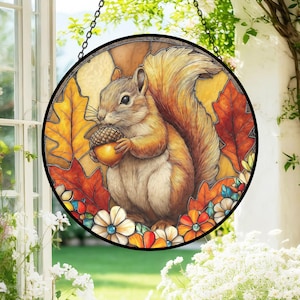 Könnte beinhalten: Rundes Buntglasfenster mit einer detaillierten Illustration eines Eichhörnchens, das eine Eichel hält. Das Eichhörnchen ist von Herbstblättern und Blumen in Orange-, Gelb- und Rottönen umgeben. Eine schwarze Metallkette ist oben befestigt.