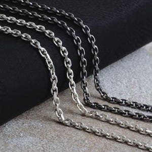 Könnte beinhalten: Nahaufnahme von vier silbernen Halsketten mit ovalen Gliedern. Die Ketten variieren in der Farbe von hellem Silber bis Dunkelgrau, mit einem schwarzen Hintergrund und einer grauen Oberfläche.