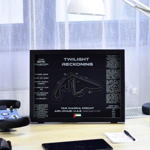 Könnte beinhalten: Ein gerahmter Druck aus der "GPX Collection" mit dem Yas Marina Circuit in Abu Dhabi. Der schwarze Druck enthält das Streckenlayout, den Text "Twilight Reckoning" und Renndetails. Der Druck wird auf einem Holztisch angezeigt.