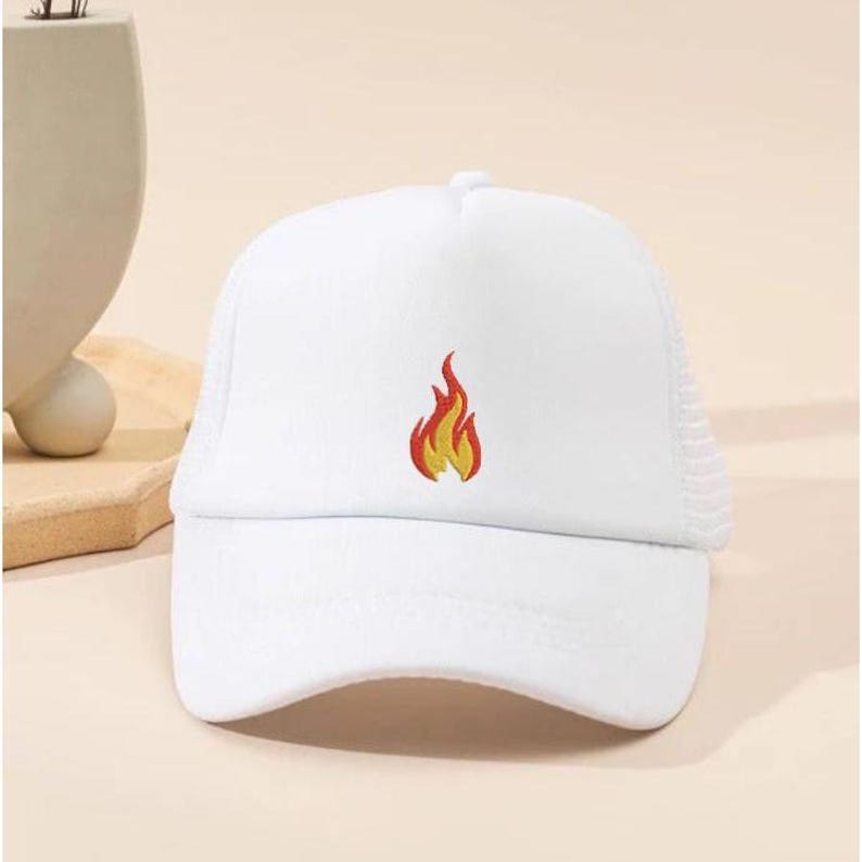 Puede incluir: Gorra de camionero blanca con una llama bordada en la parte delantera. El dise&ntilde;o de la llama presenta colores rojo y amarillo. La gorra tiene una parte trasera de malla y una visera curva.