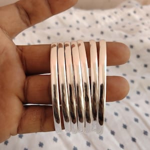 Peut inclure: Ensemble de sept bracelets de couleur argentée brillante. Les bracelets sont lisses et de forme arrondie. Ils sont présentés sur un fond blanc avec un motif discret.