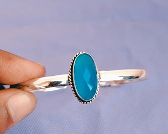 Könnte beinhalten: Ein silbernes Armband mit einem großen, ovalen, facettierten, leuchtend blauen Edelstein. Der Edelstein ist in einer dekorativen, strukturierten Lünette gefasst. Das Armband hat ein schlichtes, poliertes Band.