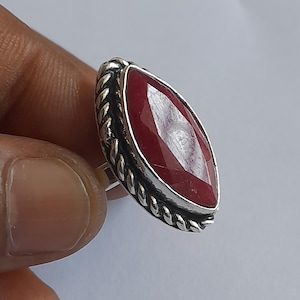 Puede incluir: Anillo de plata con una gran gema de rubí facetada en forma de marquesa. El rubí es de color rojo intenso y está engastado en un bisel de plata. El anillo tiene un diseño de cuerda trenzada alrededor de la gema.