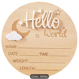 May include: A round wooden baby announcement sign with the words "Hello World" in white script. The sign includes a crescent moon, stars, and a cloud. It has spaces to write the baby's name, date, time, weight, and length.