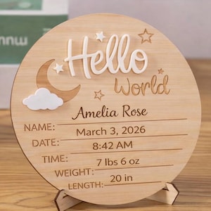 May include: Wooden birth announcement sign with the words "Hello World" and the name "Amelia Rose." The sign includes the date, time, weight (7 lbs 6 oz), and length (20 in) of the baby. The sign is supported by a wooden stand.