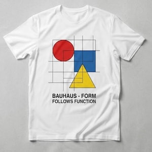 May include: White t-shirt featuring a geometric design with a red circle, blue square, and yellow triangle on a grid. The text "BAUHAUS - FORM FOLLOWS FUNCTION" is printed below the shapes. The shirt is made of a soft material.