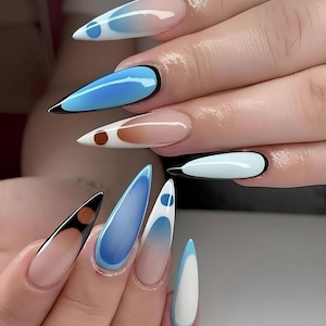 Puede incluir: Primer plano de una mano que muestra uñas acrílicas largas y puntiagudas. Las uñas presentan varios diseños, incluyendo degradados azules, blancos y marrones, y contornos negros. Algunas uñas tienen acentos circulares, creando un aspecto moderno y artístico.