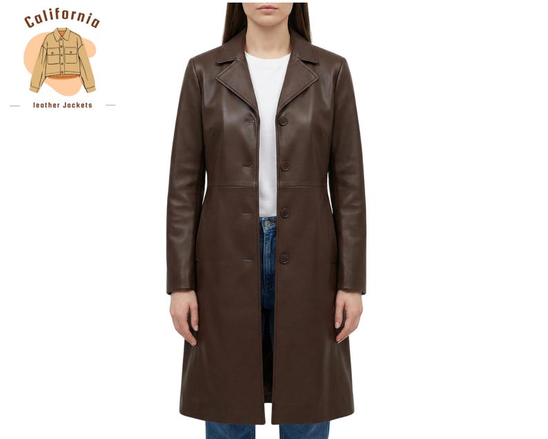 May include: A long, brown leather coat with a button-up front. The coat has a classic lapel collar and a tailored fit. The model is wearing a white t-shirt and blue jeans underneath. The coat is from California Leather Jackets.
