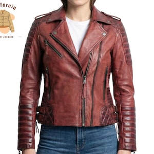 May include: A distressed burgundy leather jacket with a classic asymmetrical zip closure, quilted shoulder and elbow detailing, and multiple zippered pockets. The jacket features a notched lapel and buckle accents at the waist. The California Leather Jackets logo is in the upper left corner.