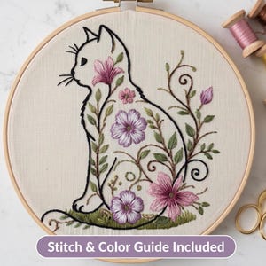 Puede incluir: Un bastidor de bordado con tela color hueso que muestra el contorno negro de un gato sentado, relleno con bordados florales morados y rosas, hojas verdes y enredaderas. El texto Stitch & Color Guide Included aparece al pie de la imagen.