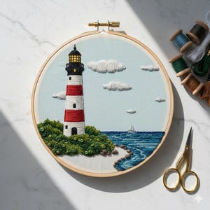 May include: Embroidered artwork depicting a lighthouse with red and white stripes, set against a light blue sky with white clouds. A sailboat sails on the blue sea, with green bushes and a wooden hoop frame. The artwork is a handcrafted piece.