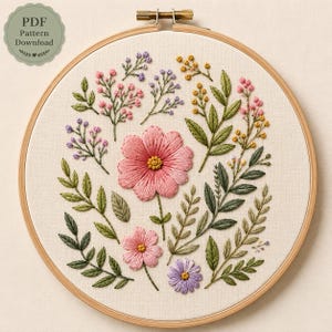 Può includere: Un telaio da ricamo circolare in legno contenente un pannello in tessuto con disegni floreali cuciti a mano. Il ricamo presenta un grande fiore centrale rosa, un fiore rosa più piccolo, un fiore viola e vari steli di foglie verdi con boccioli.