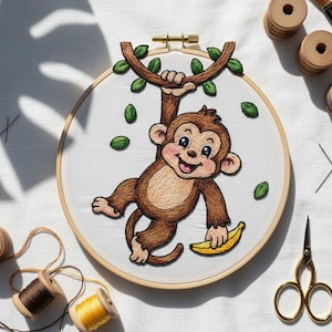 Puede incluir: Arte de aro bordado con un mono de dibujos animados sonriente colgado de una rama y sosteniendo un plátano. El mono es marrón con una cara rosa, hojas verdes y un plátano amarillo. El bordado está en un aro de madera.
