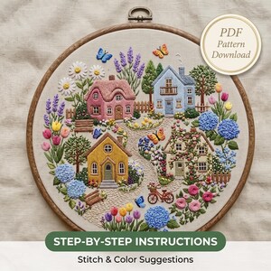 May include: An embroidery hoop featuring a colorful scene of four houses surrounded by flowers, trees, and butterflies. The design includes a pink cottage, a blue house, a yellow house, and a stone house. Text reads PDF Pattern Download.