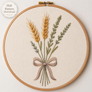 May include: An embroidery hoop containing a piece of off-white fabric with a hand-stitched design of two golden wheat stalks and two green leafy sprigs tied together with a light brown ribbon bow. The text PDF Pattern Download is visible.