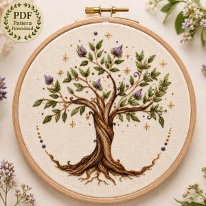 May include: A circular wooden embroidery hoop containing a fabric panel with a hand-stitched tree design. The tree features a twisted brown trunk, green leaves, purple flower buds, and gold star accents. A circular badge reads PDF Pattern Download.